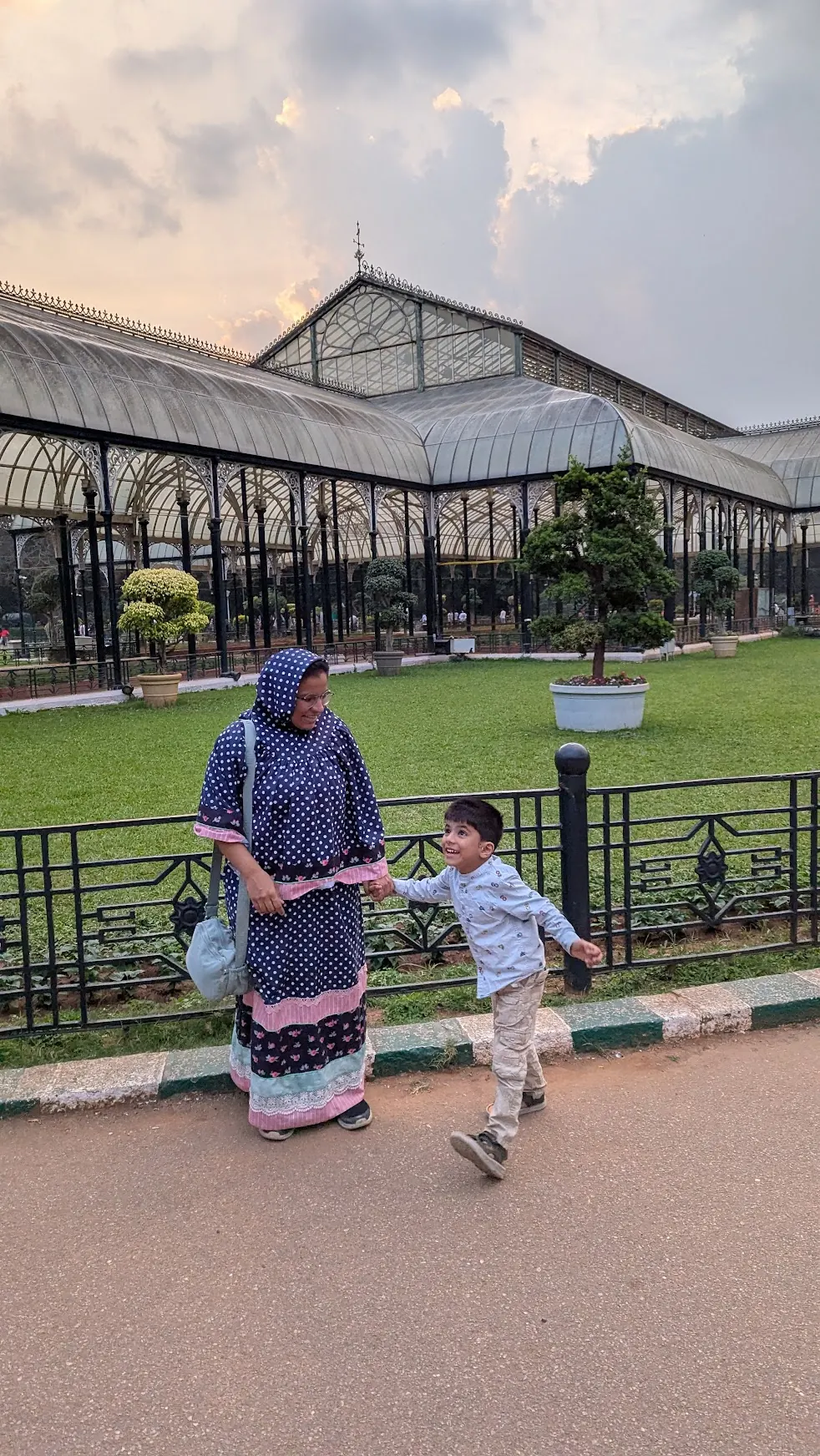 A woman and a boy walking past a glasshouse in a park